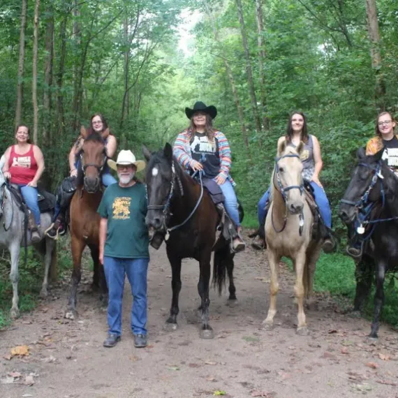 a group of people riding horses on a trail in a forest