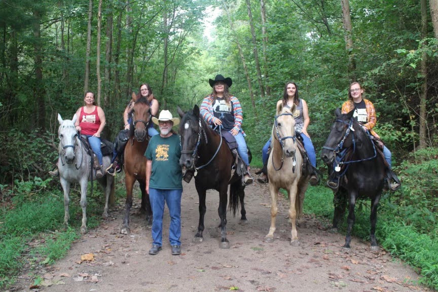 IMG_9399 a group of people riding horses on a trail in a forest